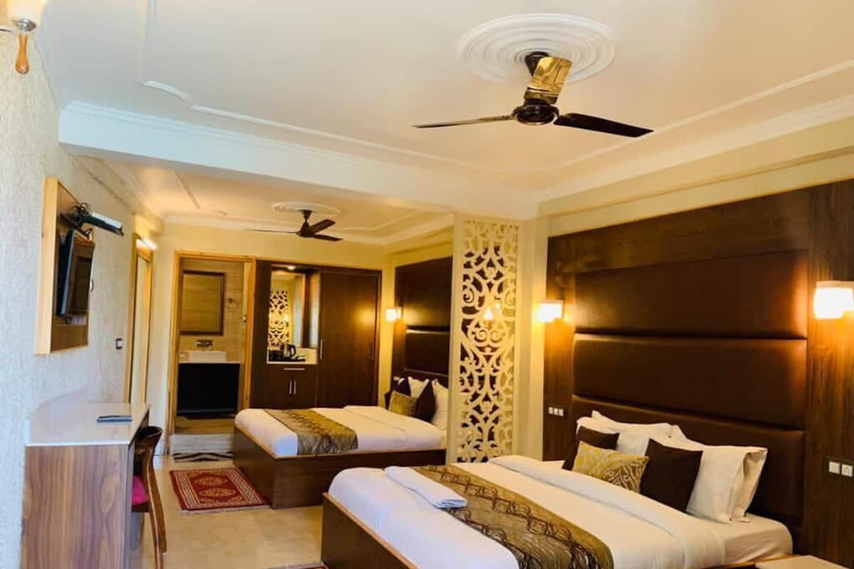 A hotel room with two beds, a desk, a chair, and a ceiling fan.
