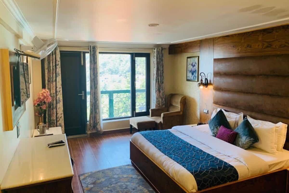A hotel room with a bed, a desk, a chair, a window, and a door.
