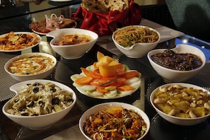 A variety of dishes on a table, including a salad with tomatoes and cucumbers, a bowl of rice with vegetables, and several other dishes. - Hotel Mongas (Dalhousie)