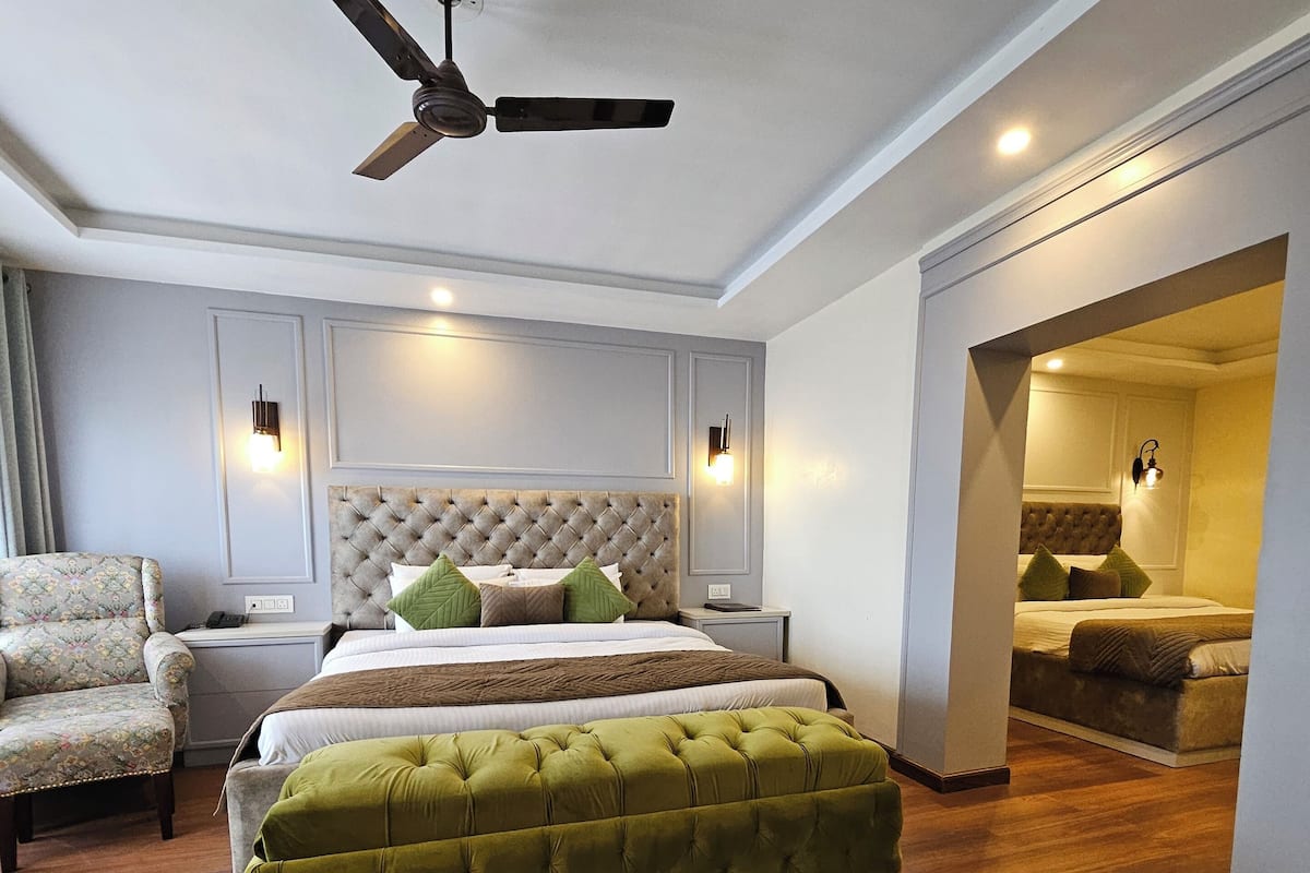 A modern bedroom with a tufted headboard, a large bed, a green upholstered bench, a ceiling fan, and a nightstand.