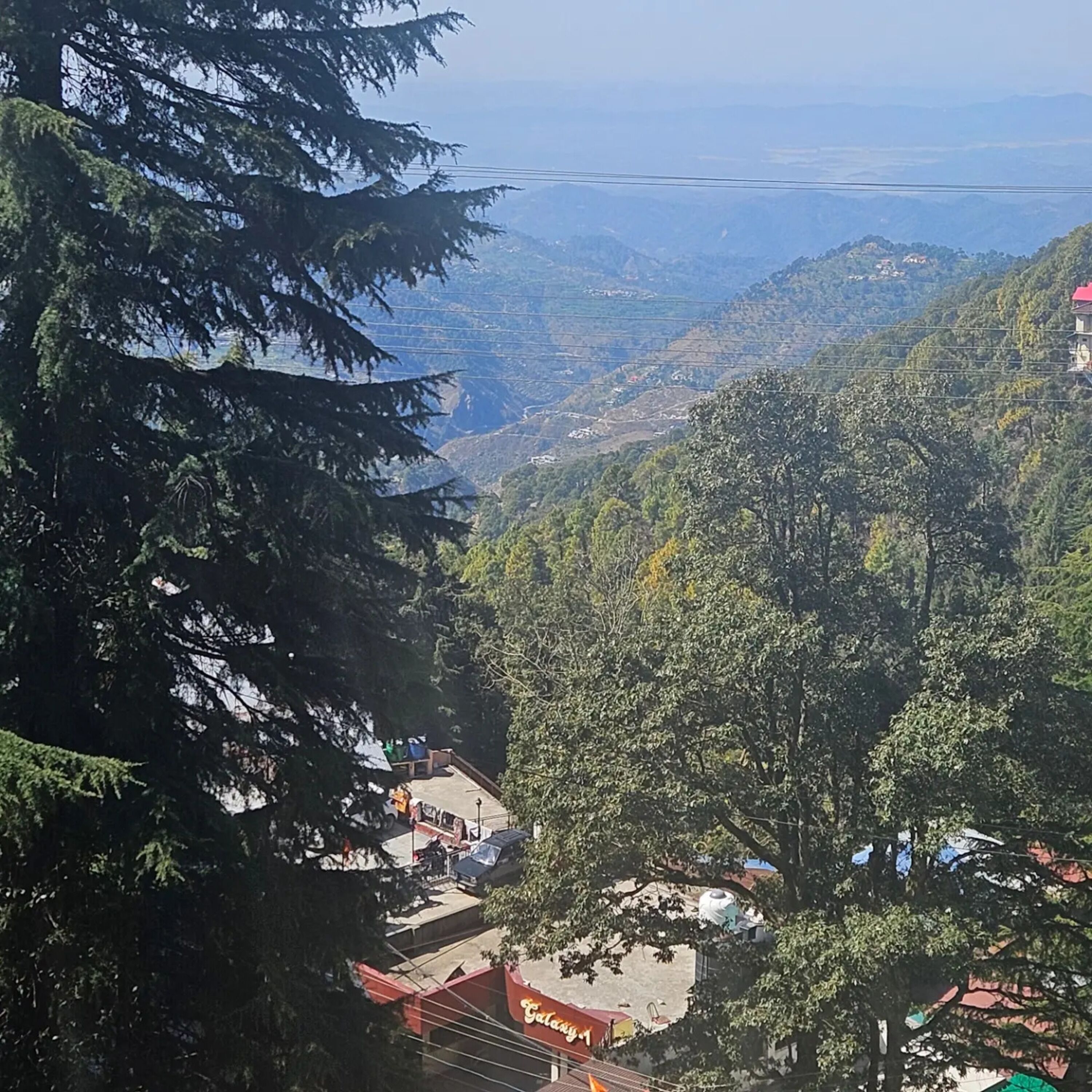 A mountainous landscape with a view of a valley. There are buildings with red roofs and a sign that reads "Cafe".