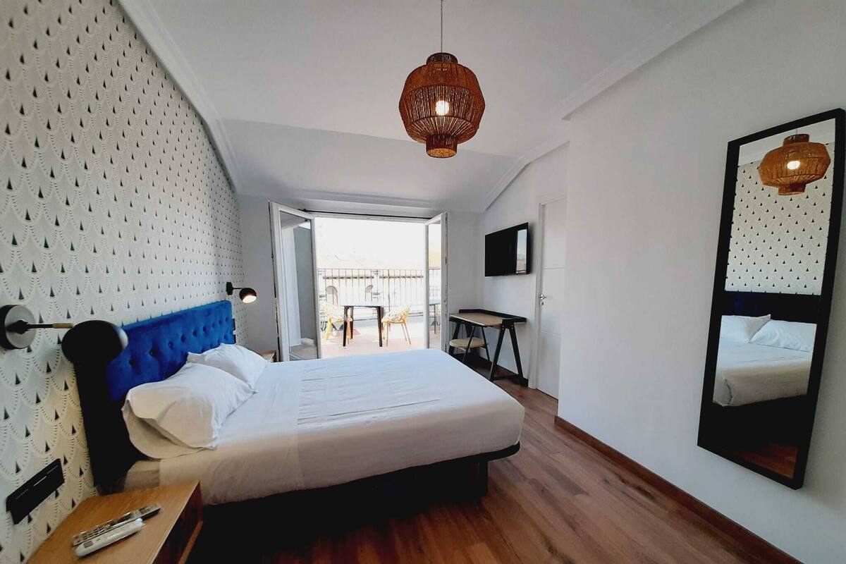Ein modernes Hotelzimmer mit einem großen Bett, Holzboden, einem blauen Kopfteil, einem an der Wand montierten Fernseher und einem großen Spiegel.