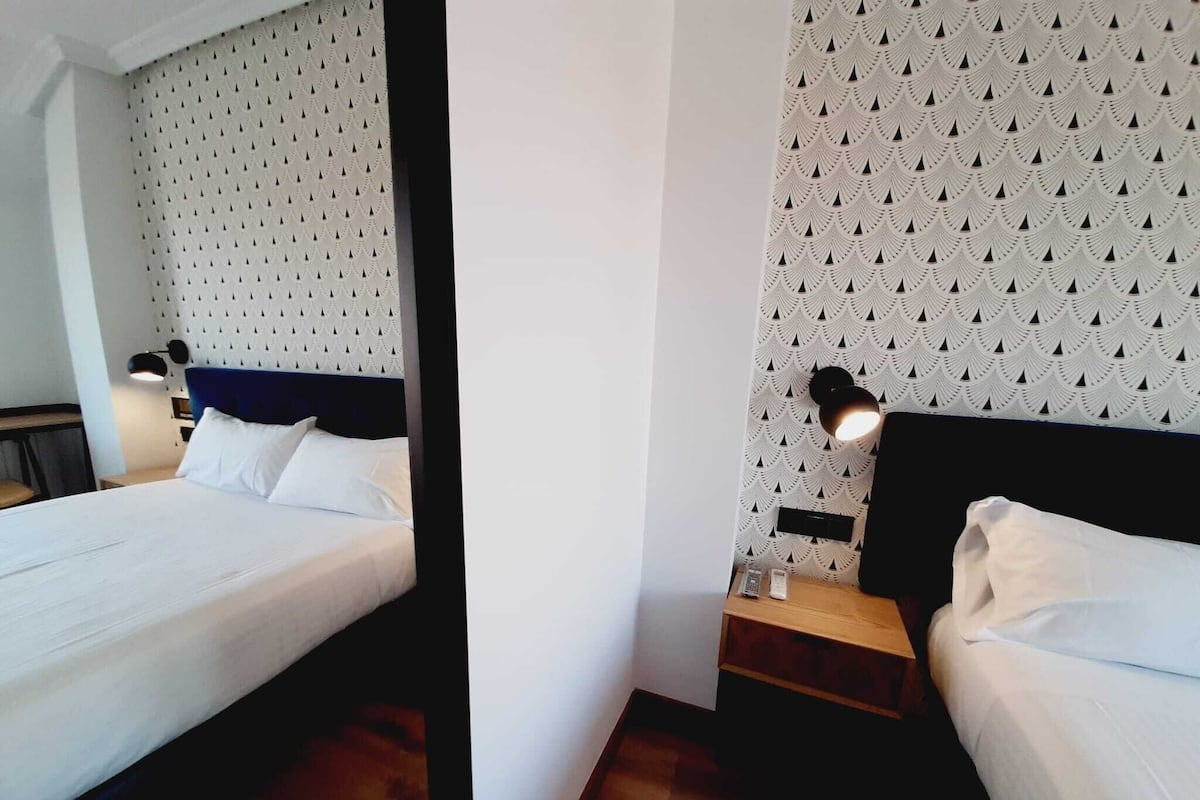 Ein Hotelzimmer mit Bett, Nachttisch, Lampe und gemustertem Wandpapier.
