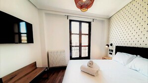 A hotel room with a large bed, a bench, a radiator, a TV mounted on the wall, and a patterned wallpaper.