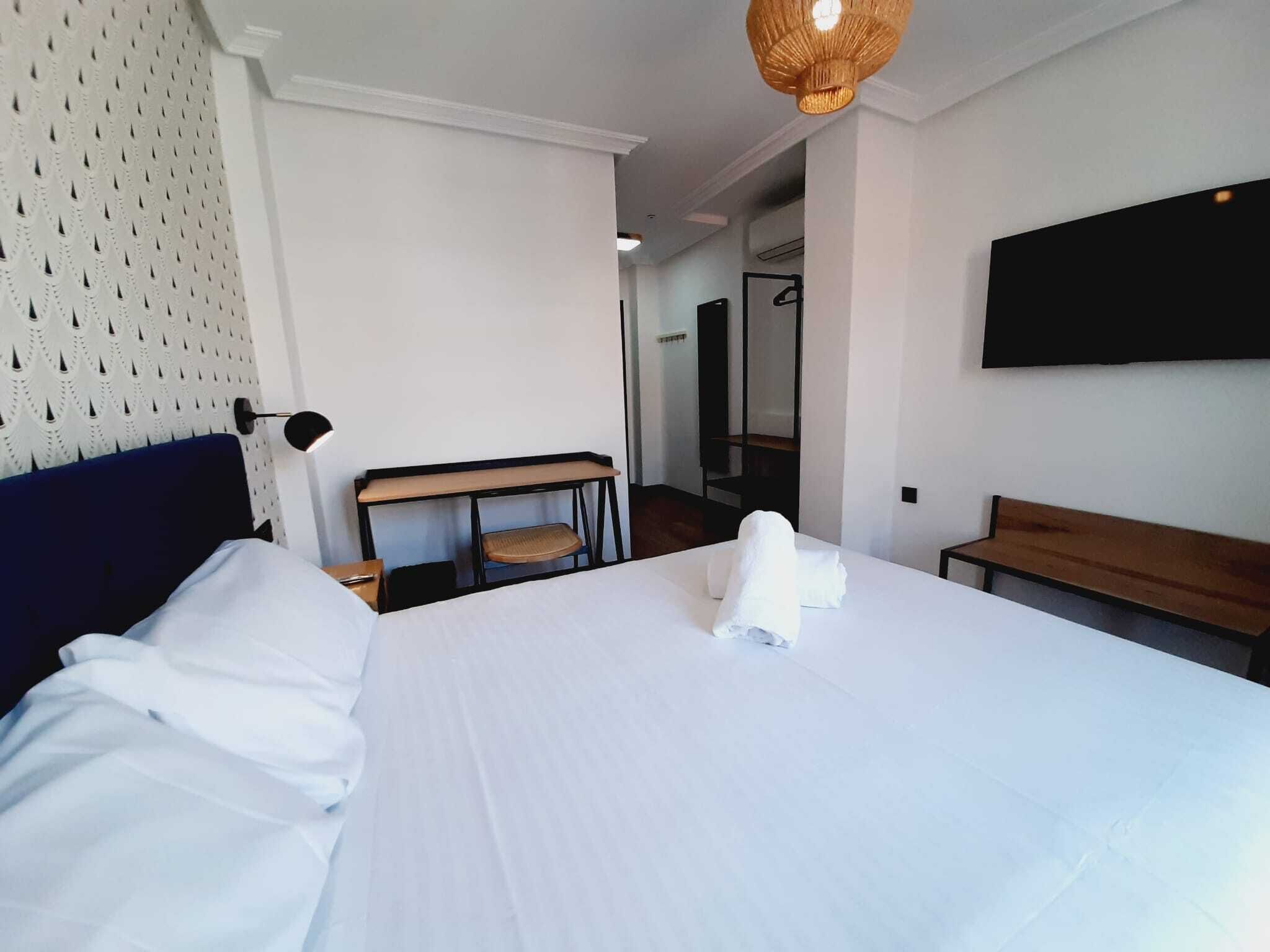 A hotel room with a large bed, a desk, a bench, and a TV on the wall.