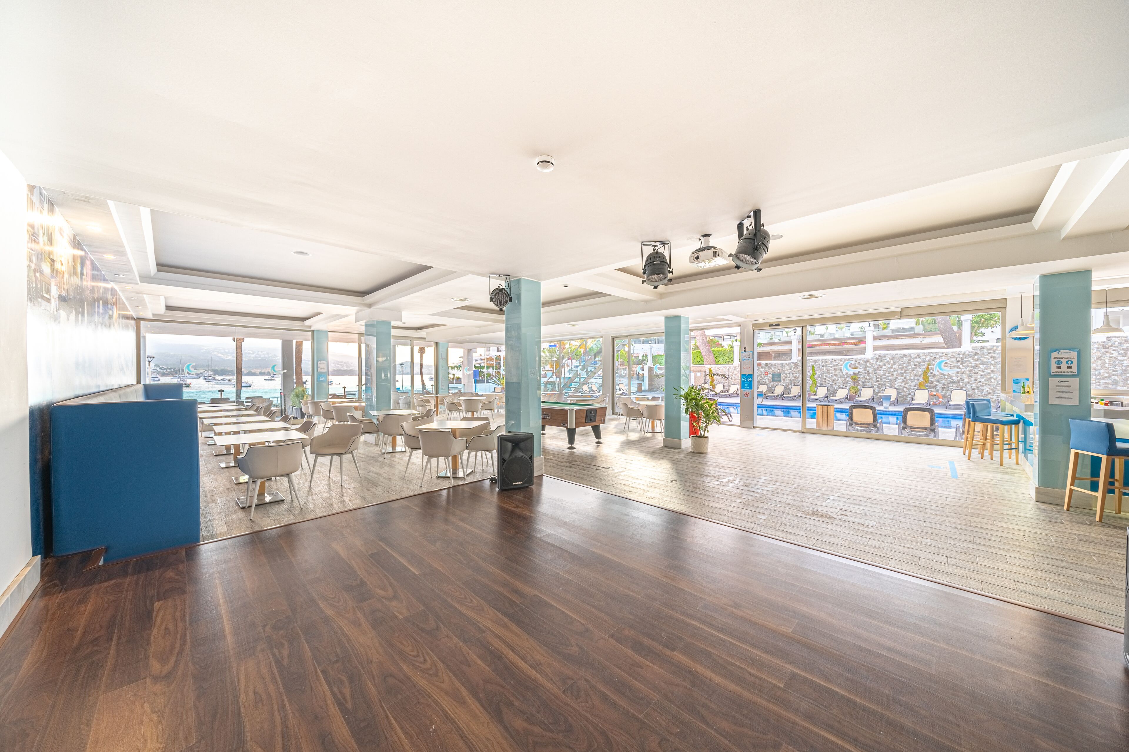 A spacious indoor area with wooden flooring, large windows, and a pool view.