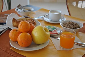 Una mesa de desayuno con naranjas, una pera, un vaso de jugo de naranja y un tazón de cereal.