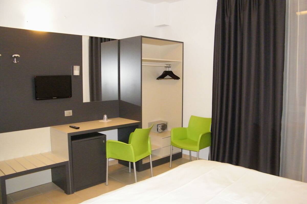 Ein Hotelzimmer mit einem Bett, einem Schreibtisch, einem Stuhl, einem Spiegel, einem Fernseher und einem Kleiderhaken.