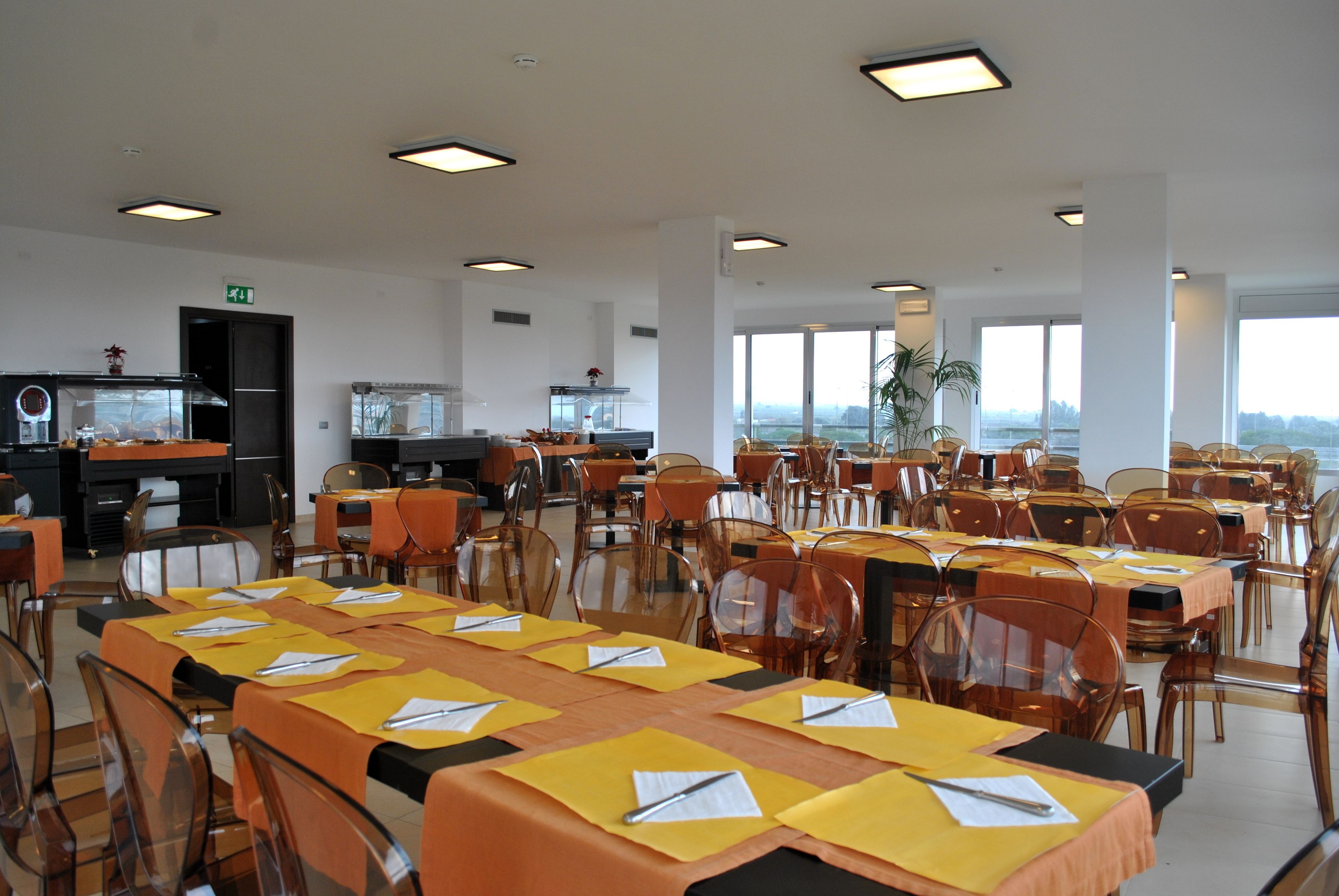 Un'ampia sala da pranzo con diversi tavoli e sedie, grandi finestre e vista sulla città.