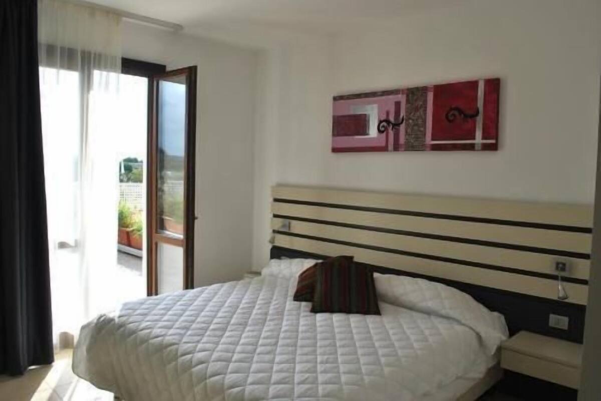 A bedroom with a bed, a nightstand, a wall-mounted artwork, and a sliding glass door to the outside.