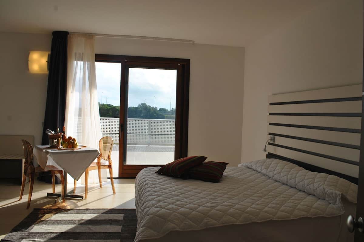 Ein Schlafzimmer mit einem Bett, einem Schreibtisch mit Stuhl, einem Tisch mit Obst und einem Balkon mit Blick.