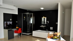 A modern hotel room with a separate dining area, a glass-enclosed shower, a large bathtub, and a white sink. - Althea Palace (Castelvetrano)