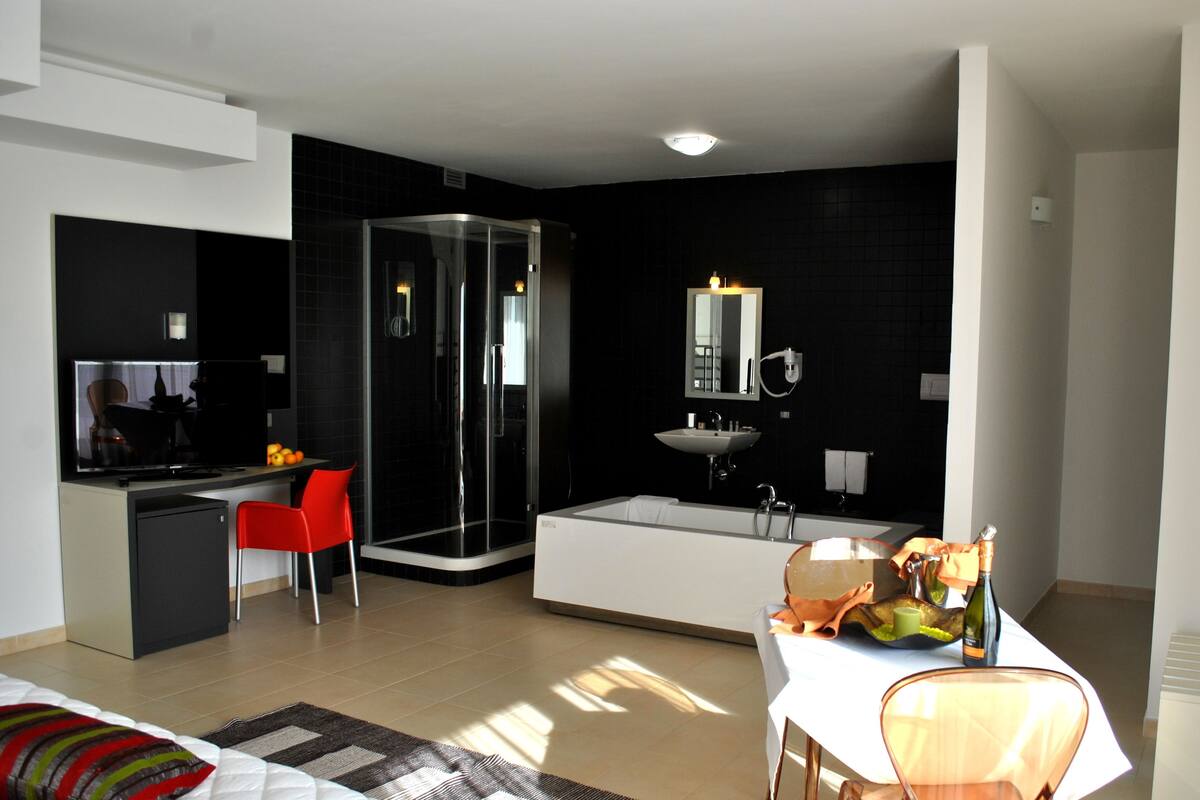 Ein modernes Hotelzimmer mit separatem Essbereich, einer Glaskabine für die Dusche, einer großzügigen Badewanne und einem weißen Waschbecken.