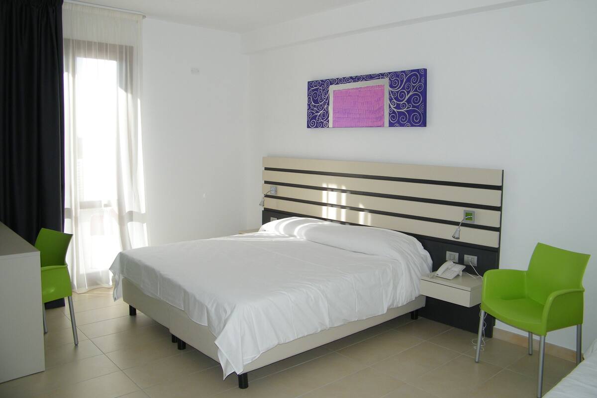 A hotel room with a bed, a nightstand, a chair, and a window with curtains.