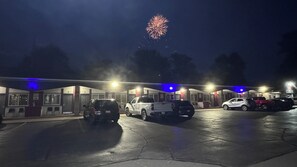 A parking lot with several cars and a building with numbered doors. - Pinconning Trail Inn Motel (Pinconning)