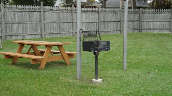 A picnic table with a grill in a grassy yard. - Pinconning Trail Inn Motel (Pinconning)