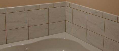 A bathroom with a corner bathtub, beige walls, and white tiled flooring.
