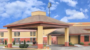 Ett Days Inn & Suites-hotell med ett takförsett utomhusområde med sittplatser, en klarblå himmel och en välskött trädgård med prydligt klippta buskar.