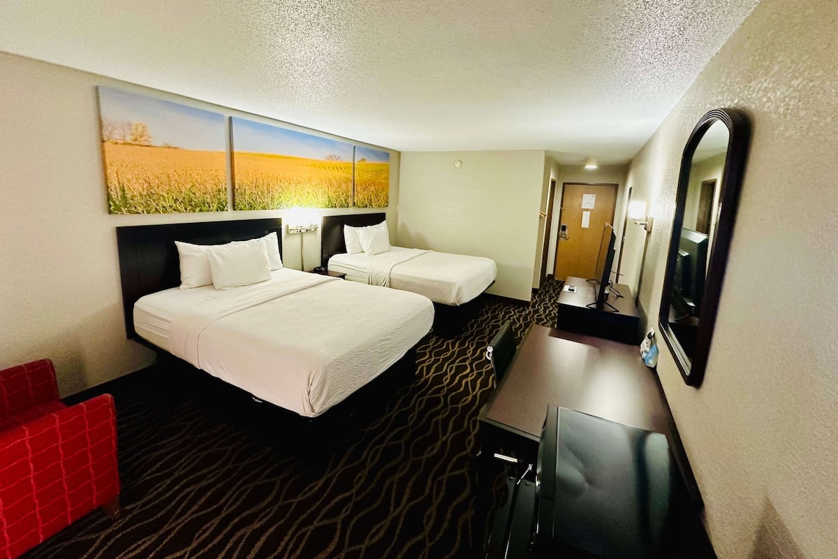 A hotel room with two beds, a desk, a red chair, and a large mirror.