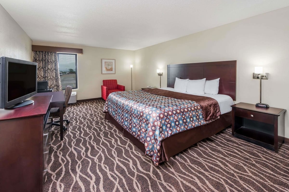 A hotel room with a bed, desk, chair, TV, and a window with curtains.