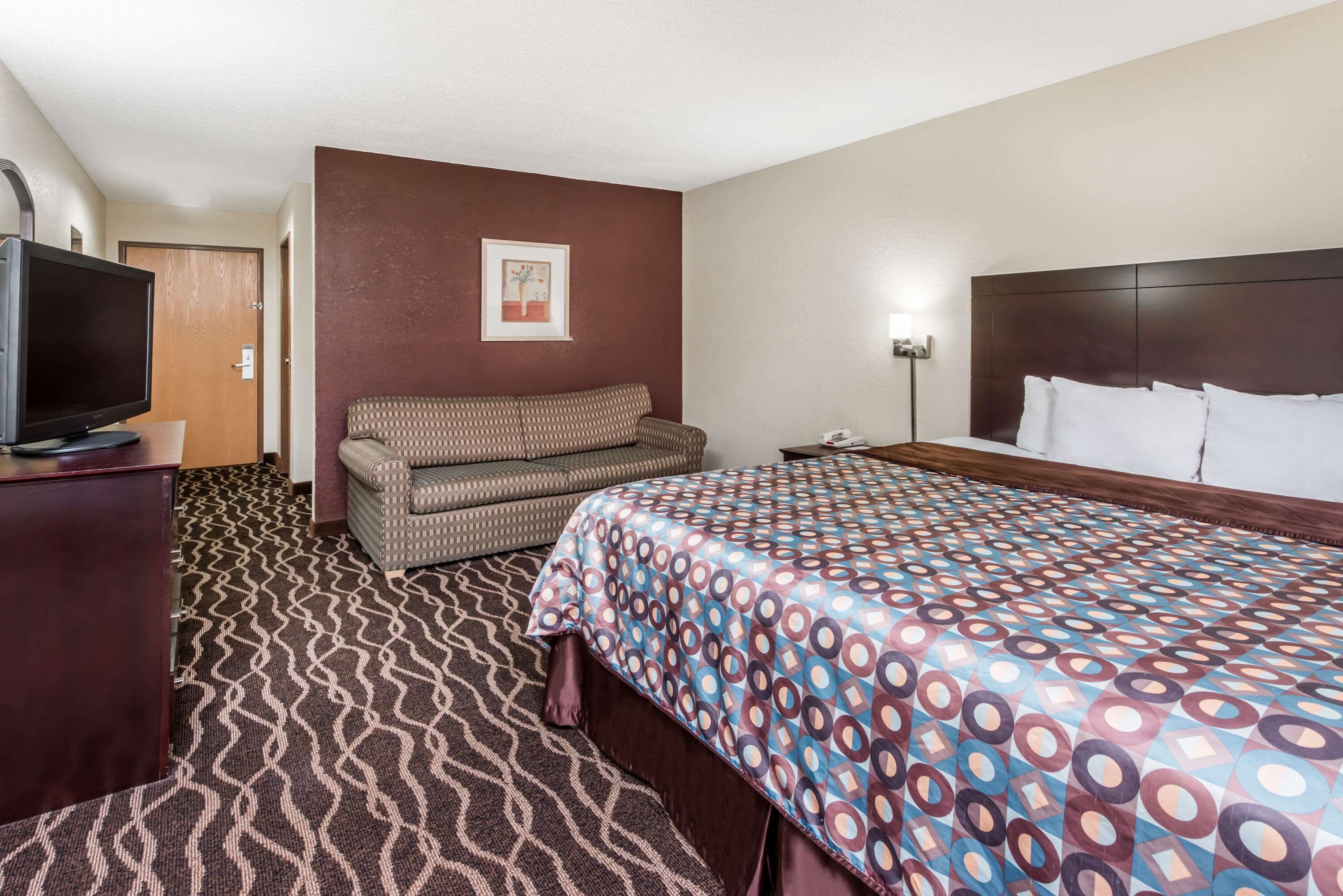 Ein Hotelzimmer mit Bett, Sofa, Fernseher und einem gemusterten Teppich.
