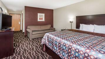 Habitación de hotel con cama, sofá, televisión y alfombra estampada.