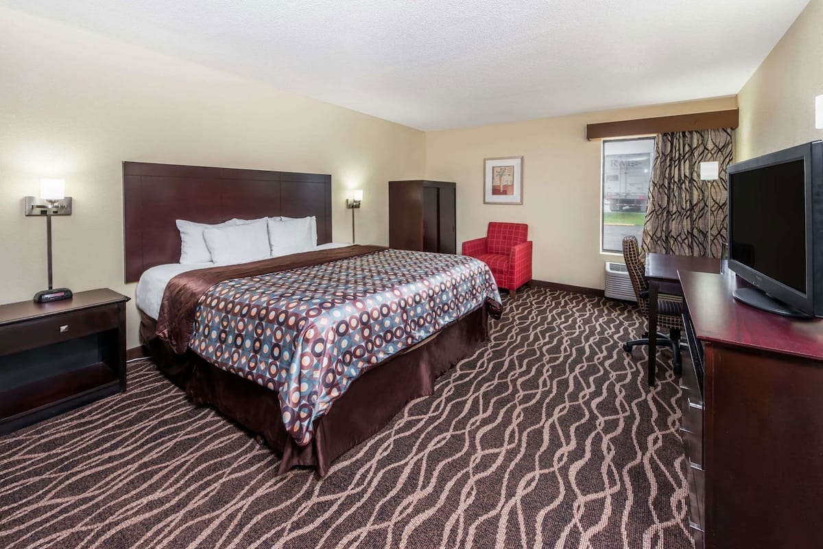 A hotel room with a large bed, a desk with a television, a chair, and a window with curtains.