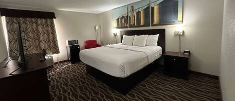 A hotel room with a large bed, a desk with a computer, a red chair, and a painting on the wall.