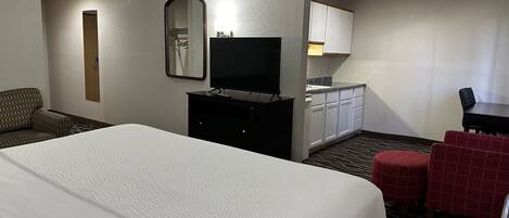 Ein Hotelzimmer mit einem großen Bett, einem Fernseher, einem Schreibtisch mit Stuhl, einem Spiegel und einer Küchenzeile.