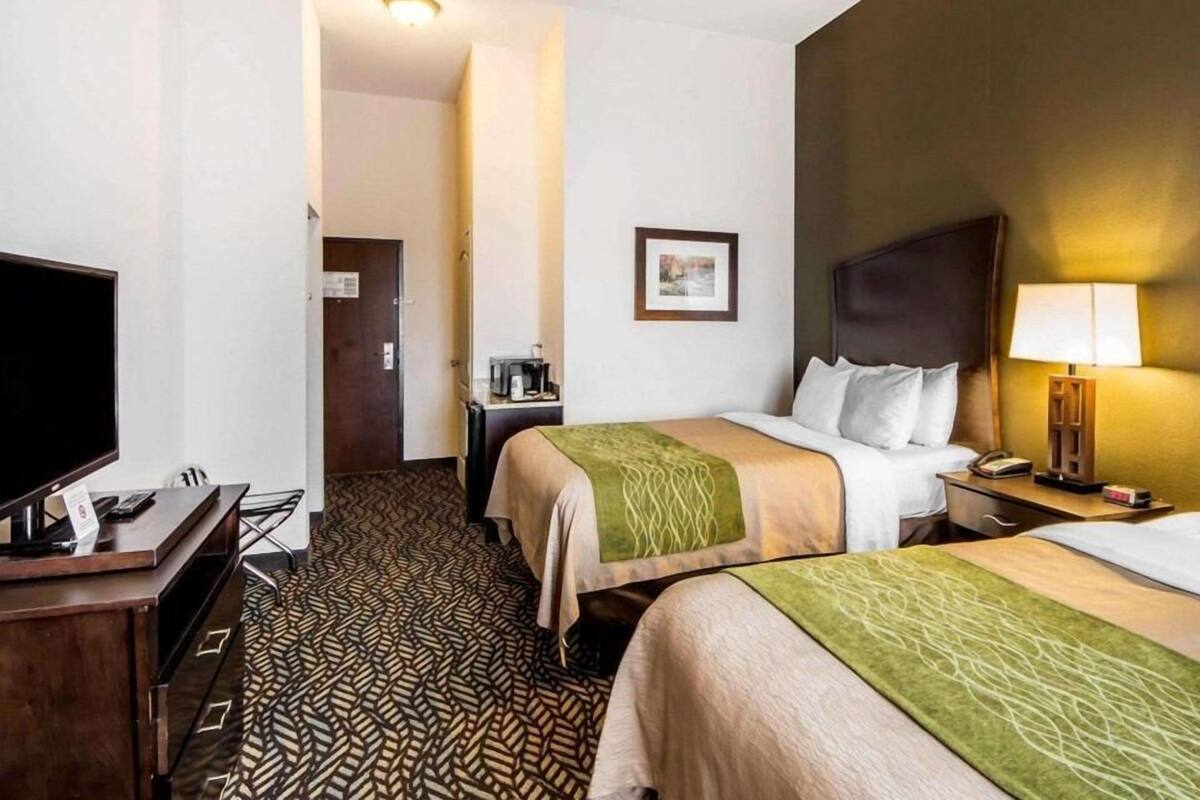 Une chambre d’hôtel avec deux lits, un bureau doté d’un téléviseur à écran plat, une lampe de bureau et un tableau encadré au mur.