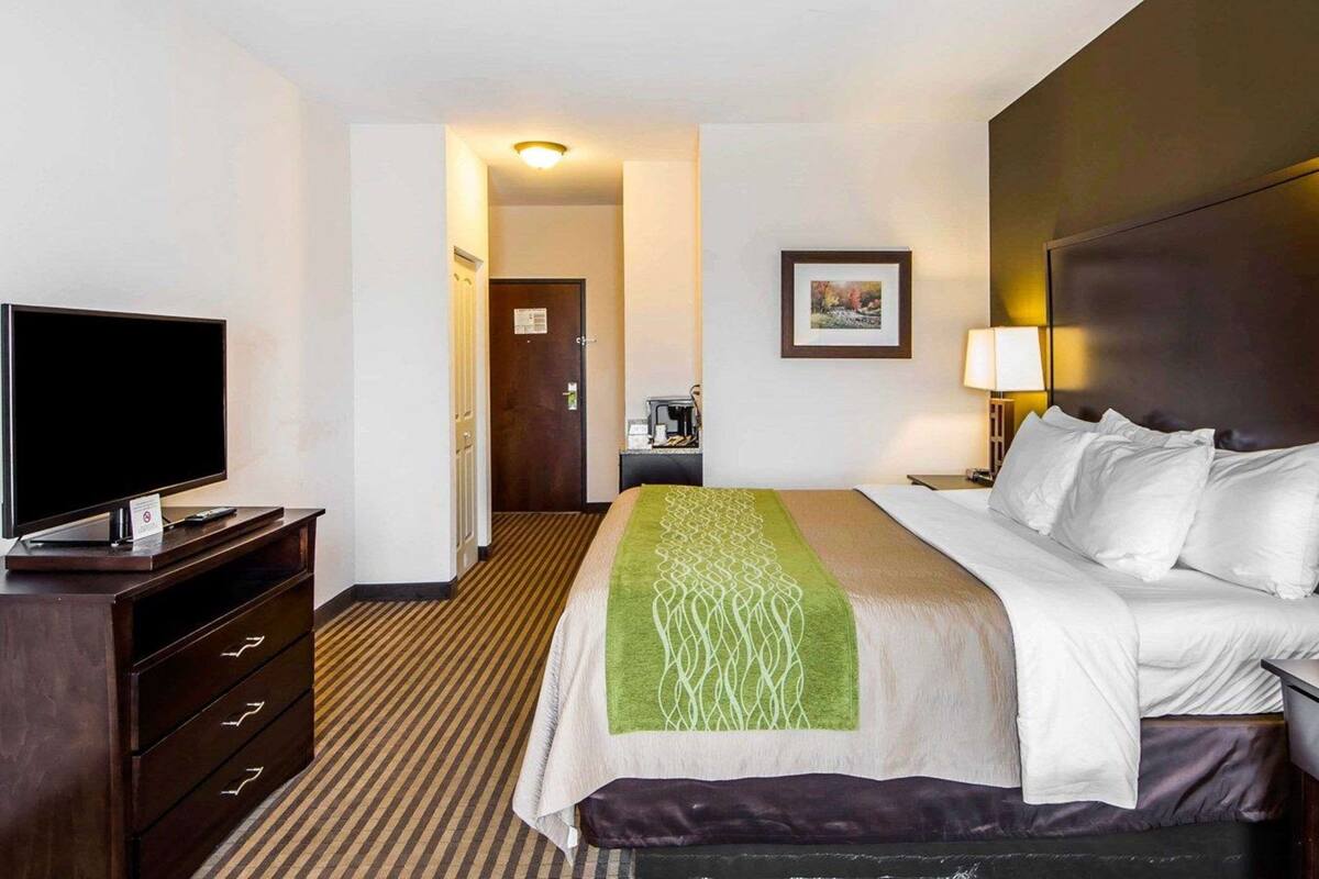 Une chambre d’hôtel avec un lit, une télévision, une commode, un bureau avec une lampe et un tableau encadré au mur.