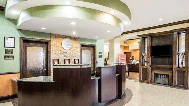 Un hall d’accueil d’hôtel avec un comptoir d’accueil incurvé, une enseigne indiquant « Comfort Inn & Suites » et un téléviseur fixé au mur.