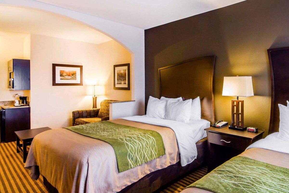 Une chambre d’hôtel avec deux lits, un bureau, une chaise, une lampe et une petite table.