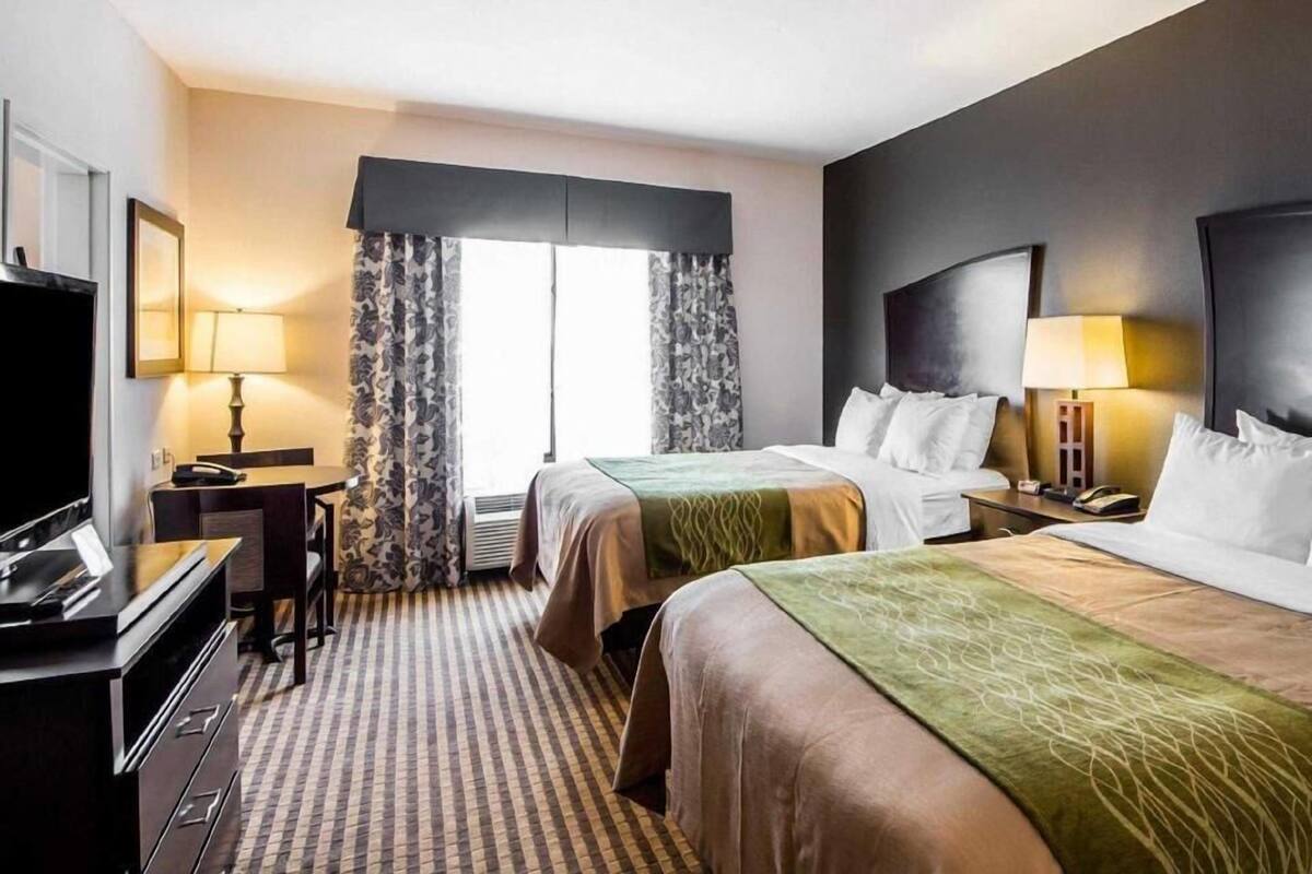 Une chambre d’hôtel avec deux lits, un bureau, une télévision et une fenêtre avec des rideaux.