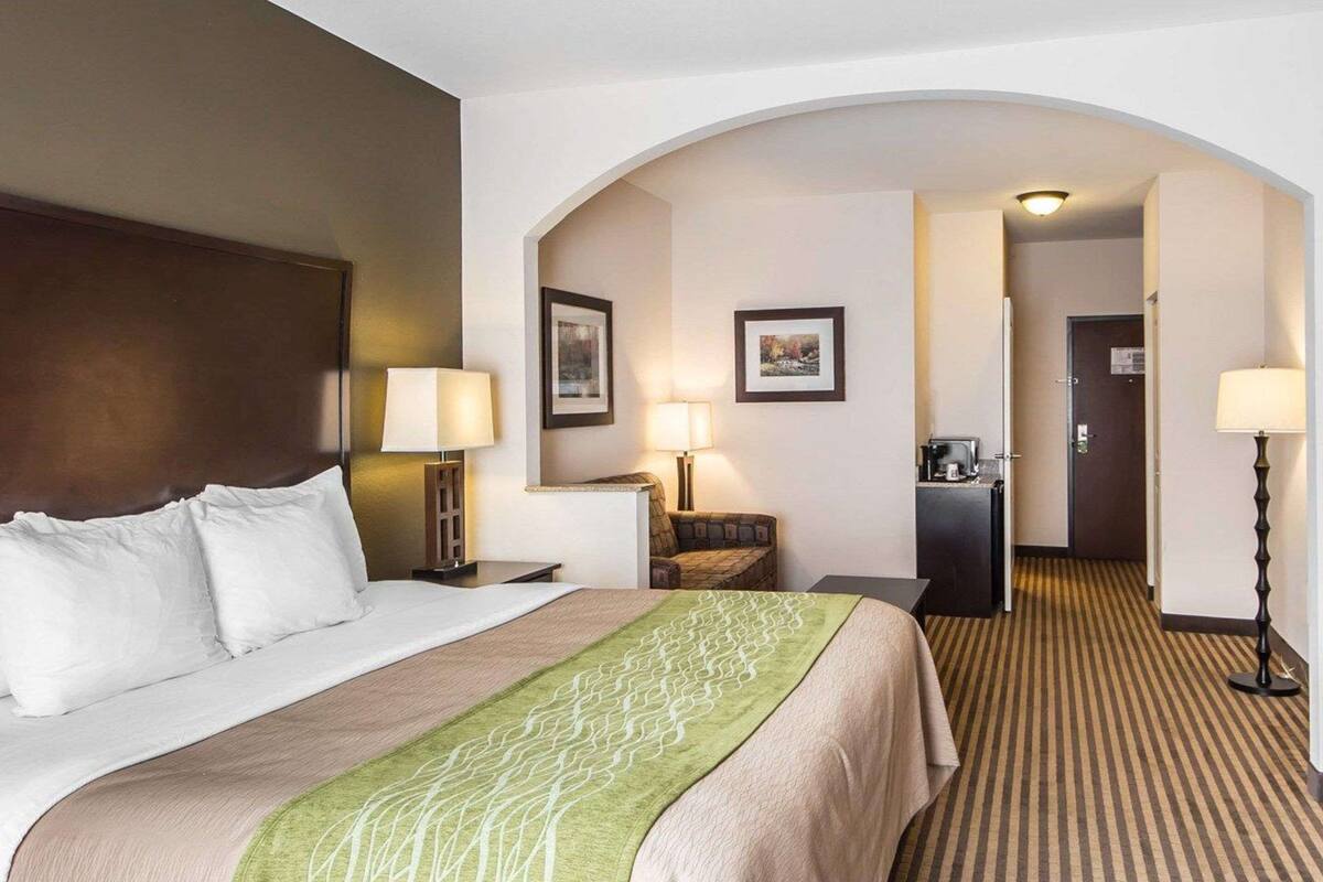 Une chambre d’hôtel avec un grand lit, deux lampes de chevet, une petite table, un bureau et une kitchenette.