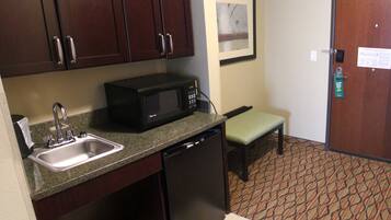 A compact hotel kitchen with dark wooden cabinets, a black microwave, a sink, and a small bench.