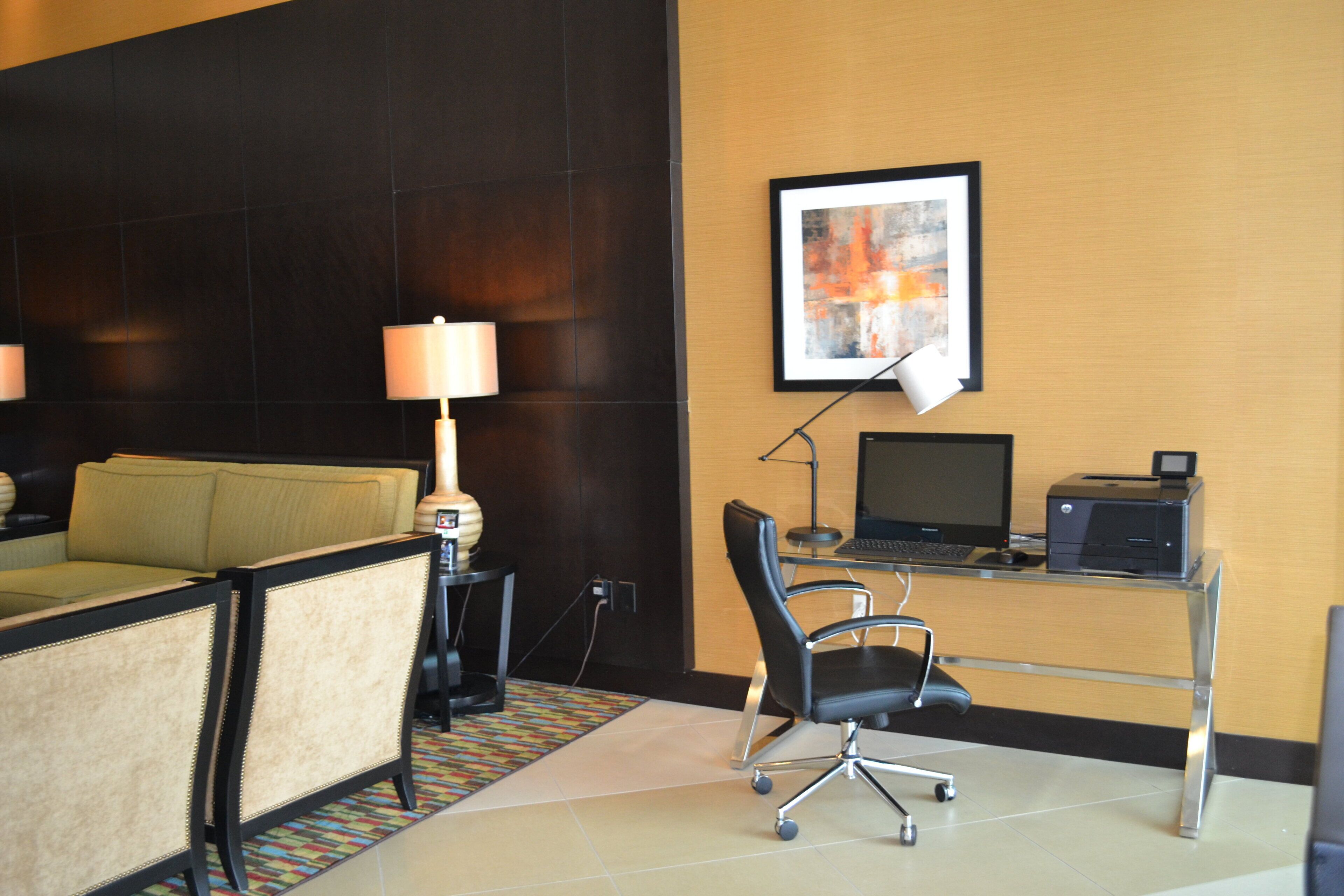 A hotel room with a sofa, a desk with a computer, a lamp, and a framed picture on the wall.