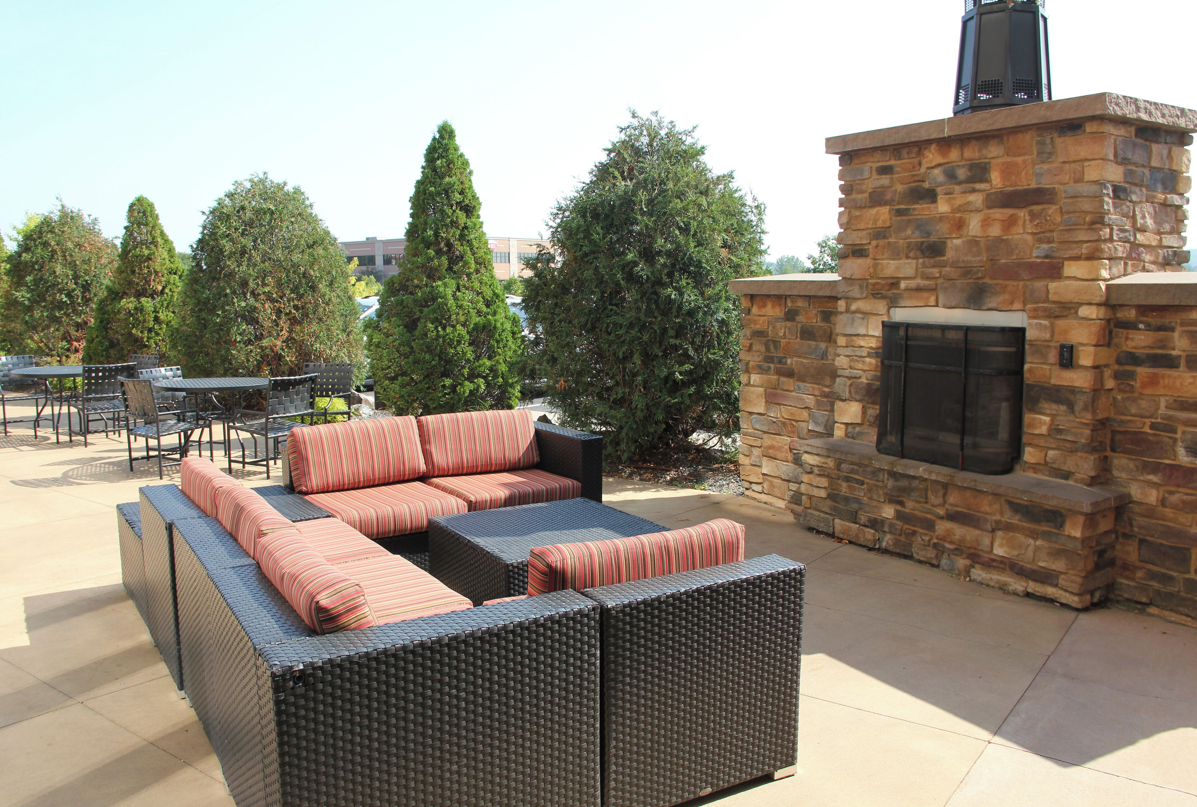 An outdoor seating area with a stone fireplace, wicker furniture, and surrounding greenery.