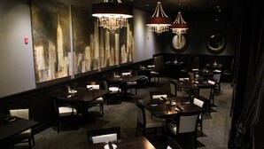 Un restaurante con varias mesas y sillas, candelabros y un cuadro de un paisaje urbano en la pared.