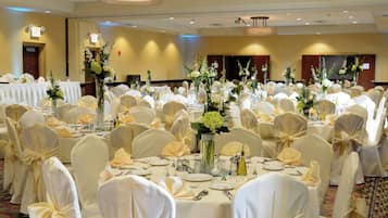 A banquet hall with round tables, white tablecloths, and chairs with bow ties.