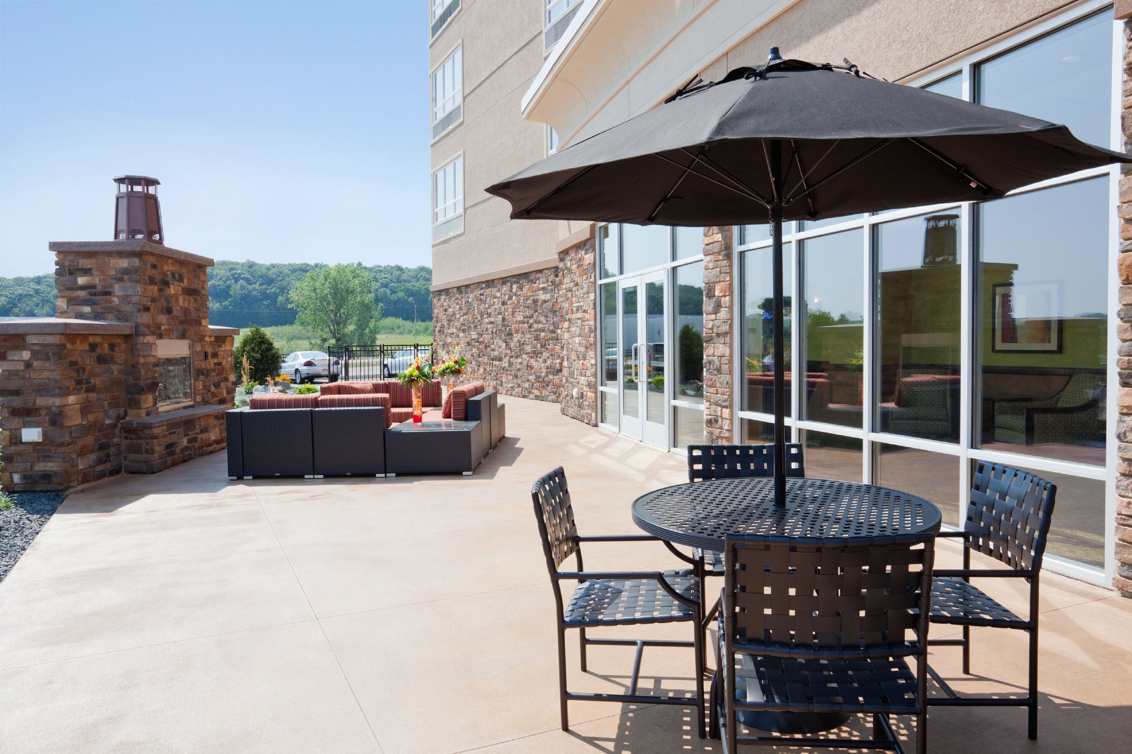 An outdoor patio with a stone fireplace, a seating area with sofas and a table, and a large umbrella.