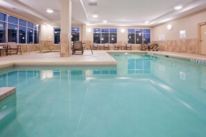 Une piscine intérieure d’hôtel dotée de plusieurs espaces aménagés pour s’asseoir et d’un poste de surveillance pour les sauveteurs.