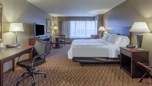 Una habitación de hotel con cama, escritorio, silla, televisor y lámparas.