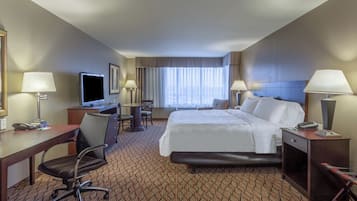 A hotel room with a bed, desk, chair, TV, and lamps.