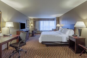Una habitación de hotel con cama, escritorio, silla, televisor y lámparas.