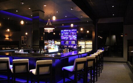 A bar area with a long counter, multiple bar stools, and a well-lit bar display.