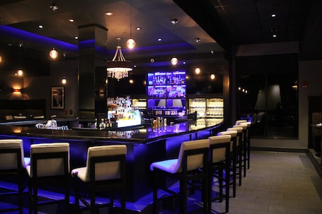 A bar area with a long counter, multiple bar stools, and a well-lit bar display.