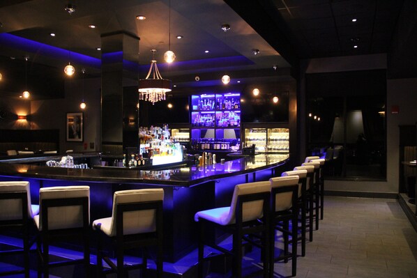 A bar area with a long counter, multiple bar stools, and a well-lit bar display. - Holiday Inn Eau Claire South I-94 by IHG (Eau Claire)