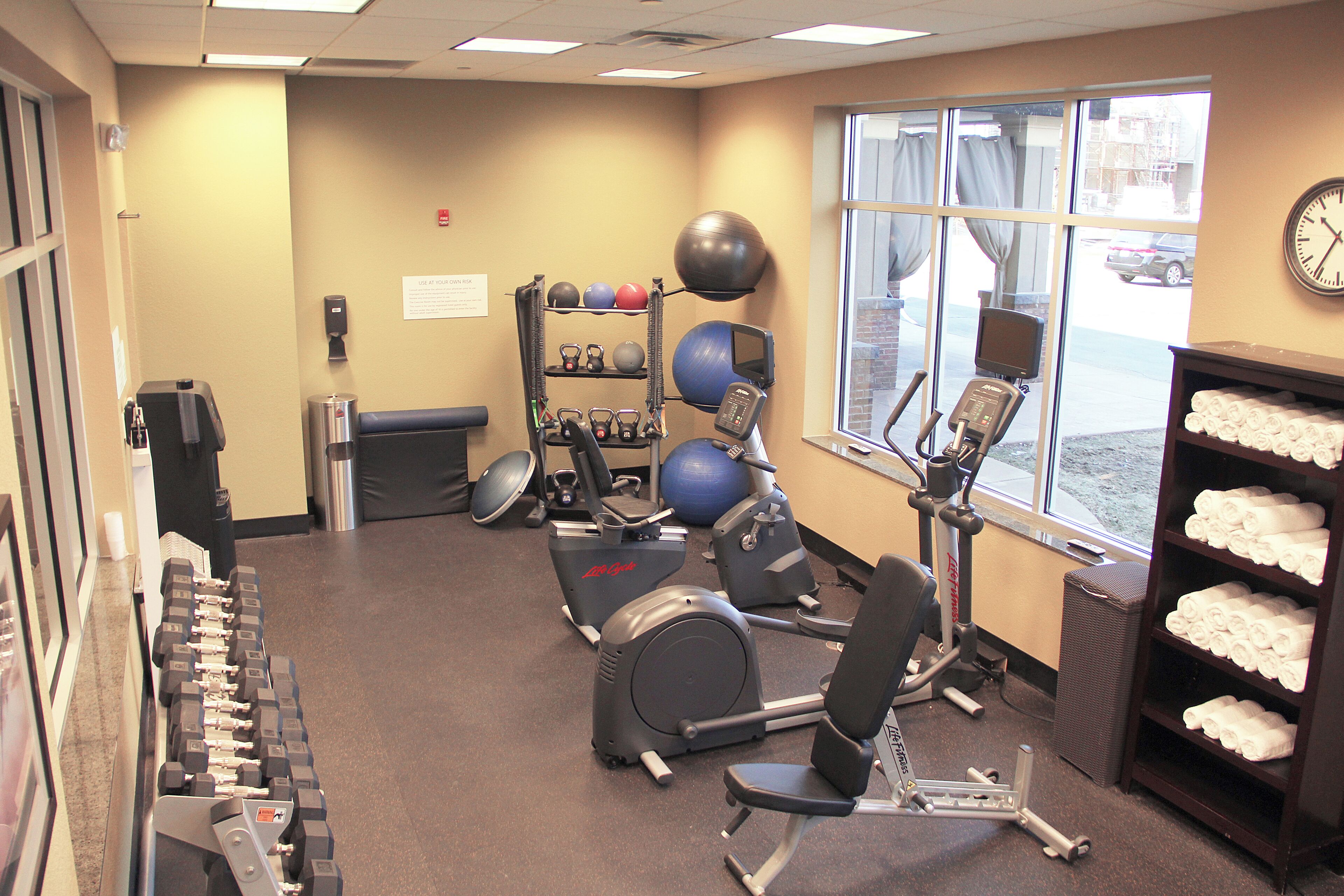 A gym with exercise equipment, a water dispenser, and a window with a view of the street.