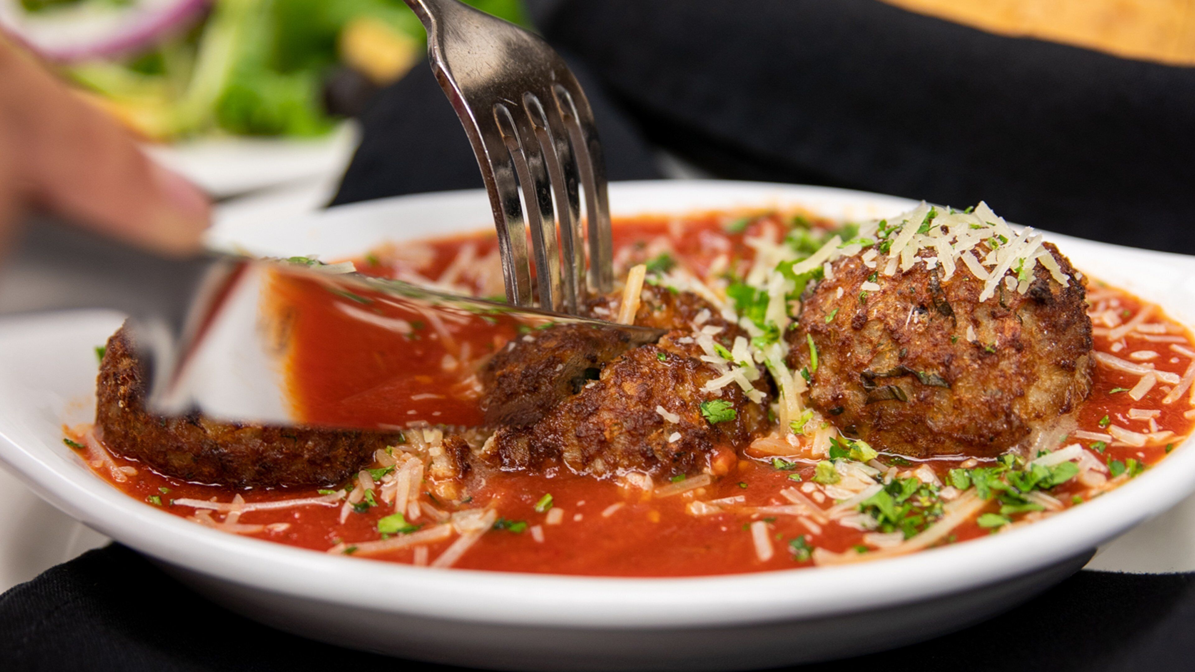 Une assiette de boulettes de viande nappées de sauce tomate, saupoudrées de fromage râpé et d’herbes aromatiques.
